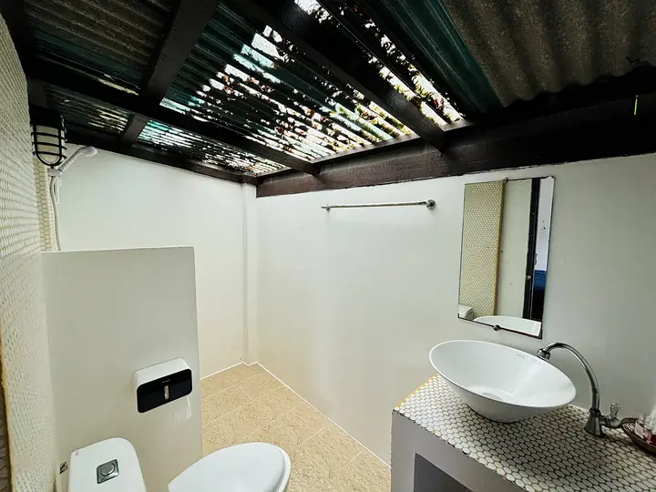 De openluchtbadkamer van een Front Sea View-bungalow, met een kom als wastafel onder een lattendak