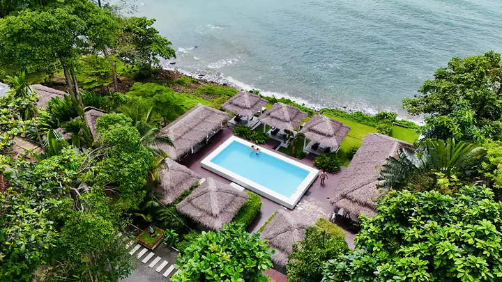 Luchtfoto van het resort aan de kust: het zwembad, de rieten sala's en de zee