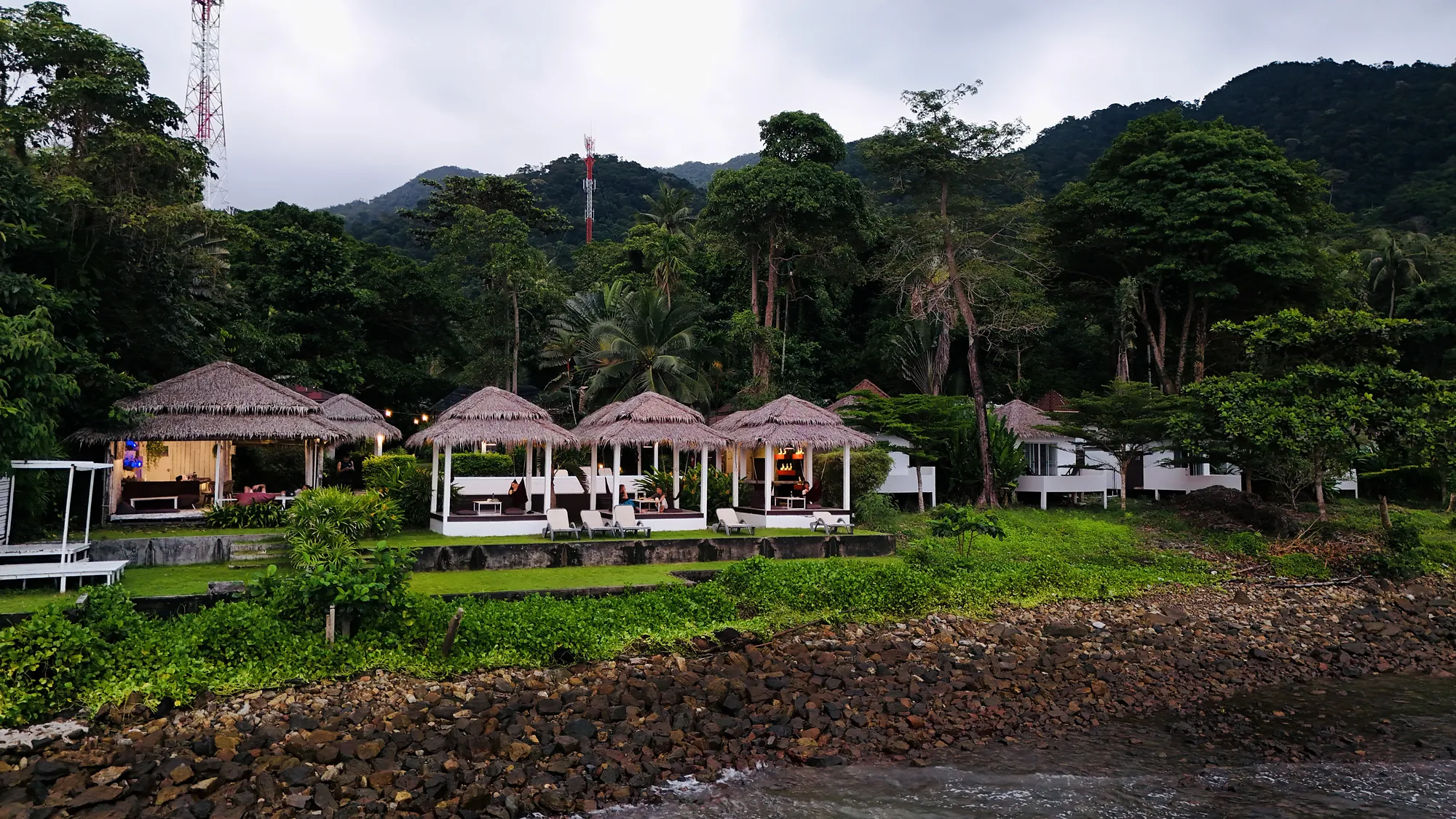 Paradise Cottage from the sea: thatched salas along the shore with the jungle and hills behind