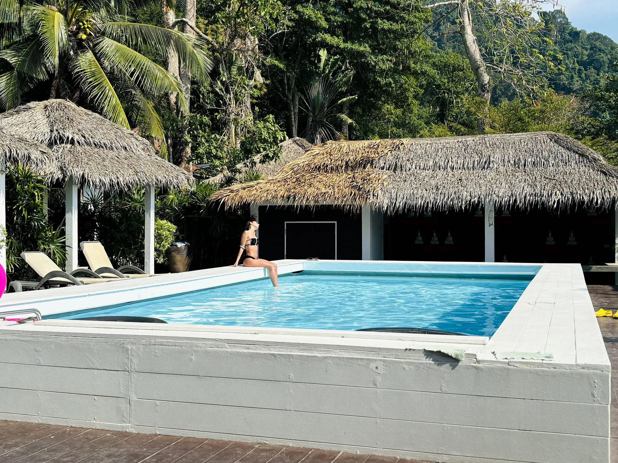 A guest on the edge of the pool in front of the thatched restaurant and the jungle