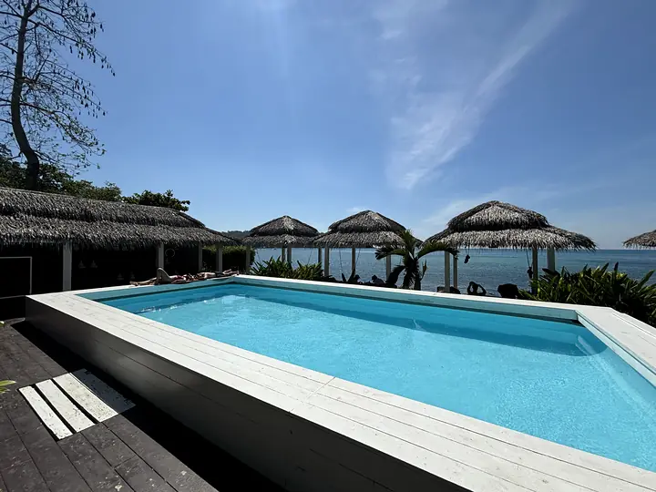 Het zwembad op het terras met rieten sala's en de zee onder een blauwe lucht