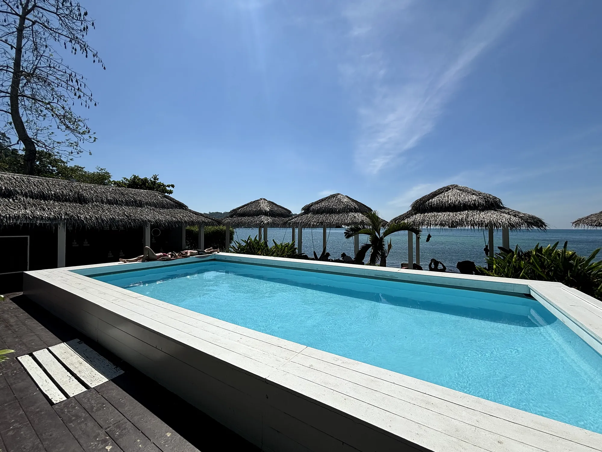 The pool on the deck with thatched salas and the sea under a blue sky