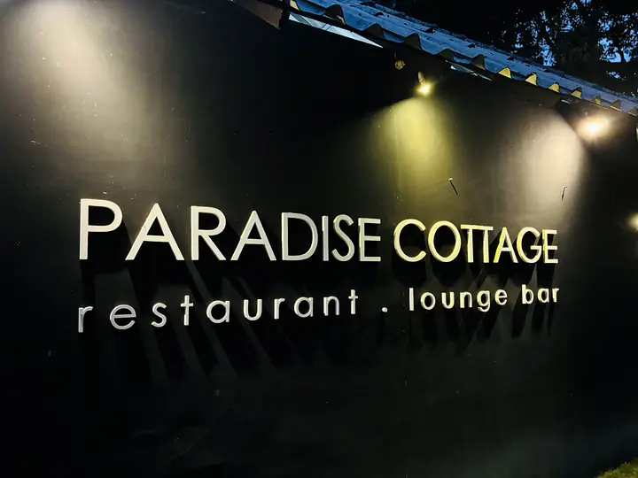 Het verlichte bord van het restaurant en de lounge bar van Paradise Cottage in de nacht